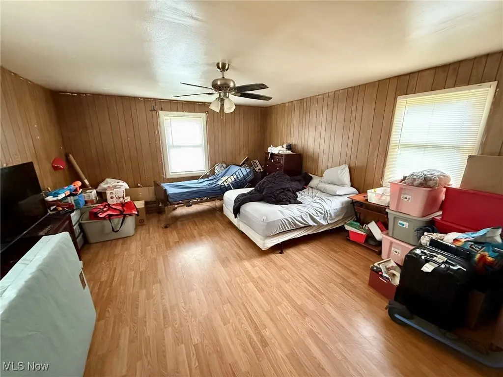 Bedroom featuring light wood finished floors, a ceiling fan, and wooden walls