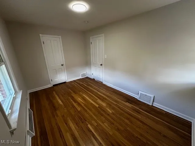 Empty room with baseboards and dark wood-type flooring