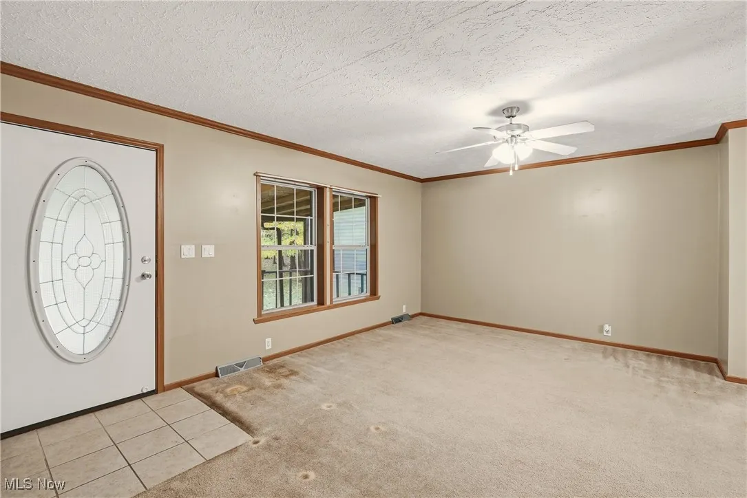 Foyer featuring light carpet, a textured ceiling, ornamental molding, ceiling fan, and light tile patterned floors