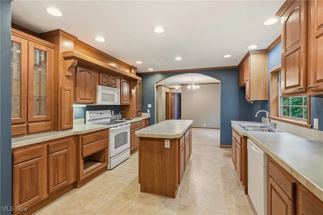 Kitchen featuring arched walkways, white appliances, a kitchen island, glass insert cabinets, and recessed lighting