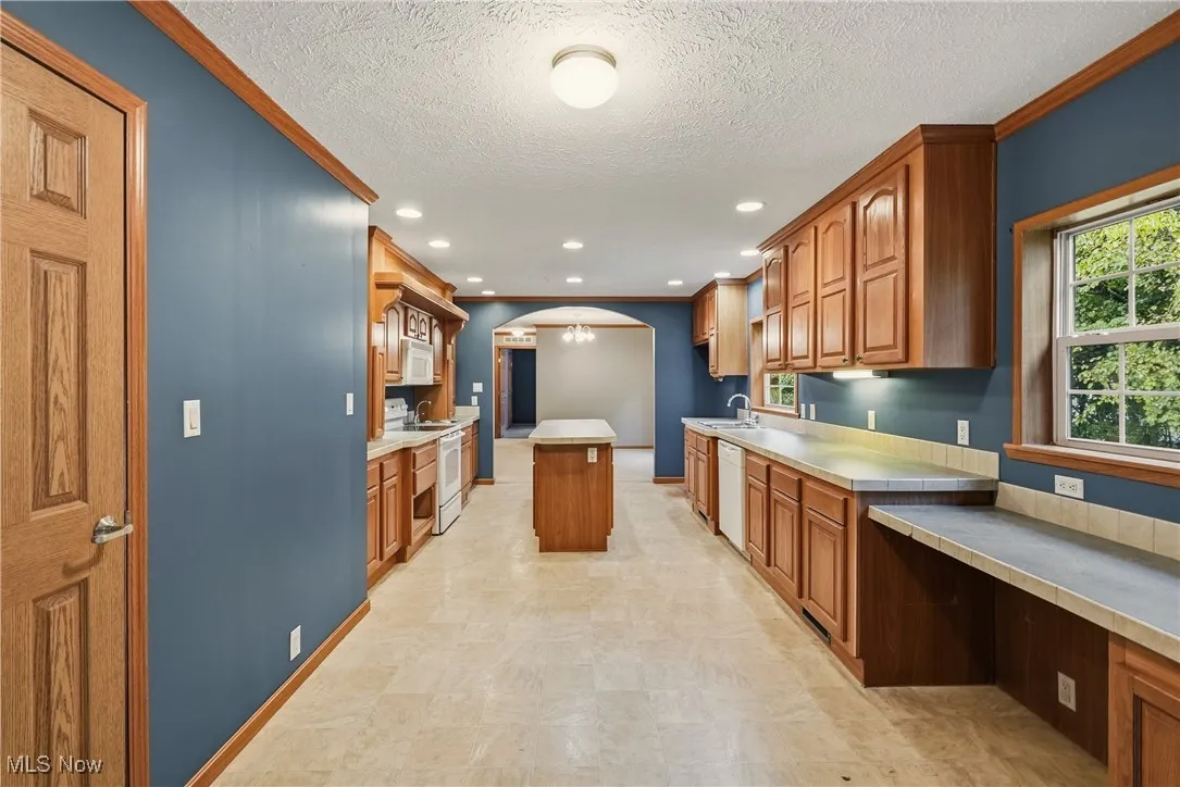Kitchen with arched walkways, ornamental molding, light countertops, brown cabinets, and a chandelier