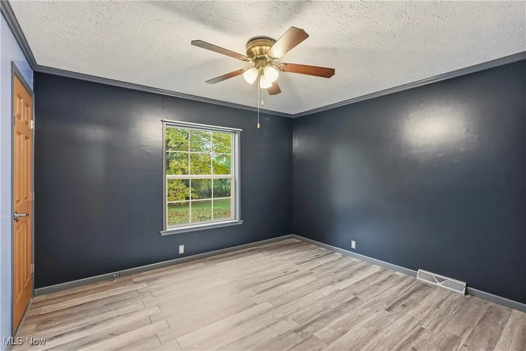 Spare room featuring light wood-style floors, a textured ceiling, and a ceiling fan