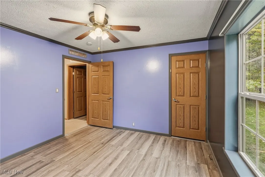 Unfurnished bedroom featuring multiple windows, ornamental molding, wood finished floors, a textured ceiling, and a ceiling fan