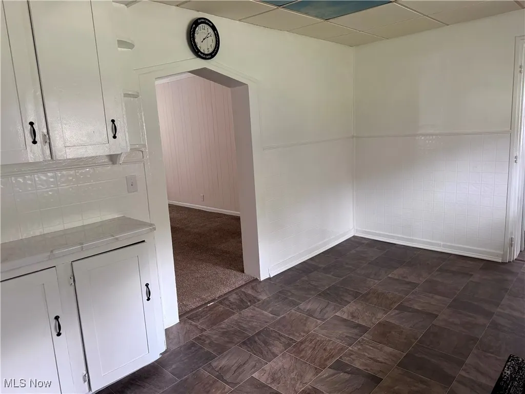 Unfurnished dining area with a drop ceiling, wainscoting, and arched walkways