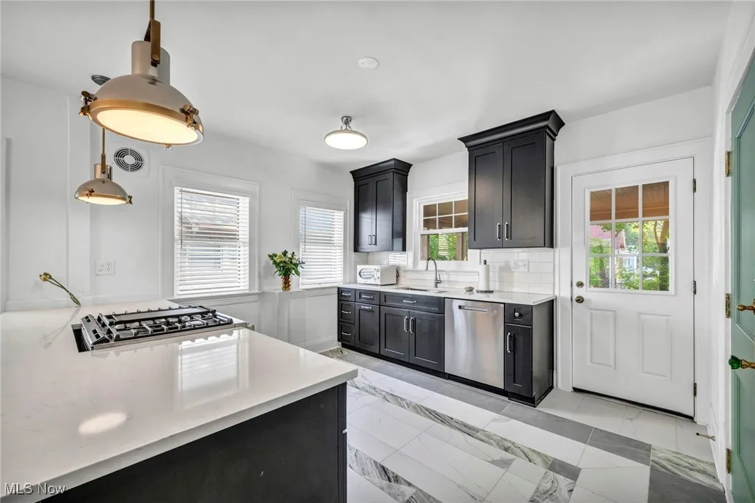 Kitchen featuring stainless steel appliances, tasteful backsplash, pendant lighting, light stone countertops, and plenty of natural light