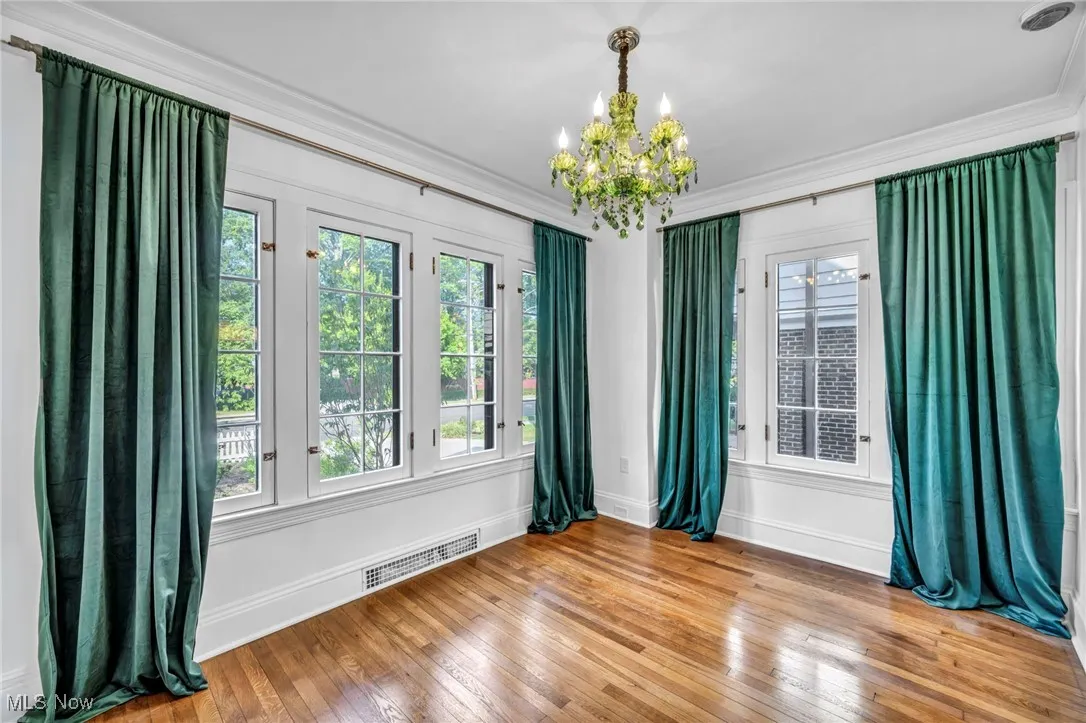 Empty room with ornamental molding, light wood finished floors, and a chandelier