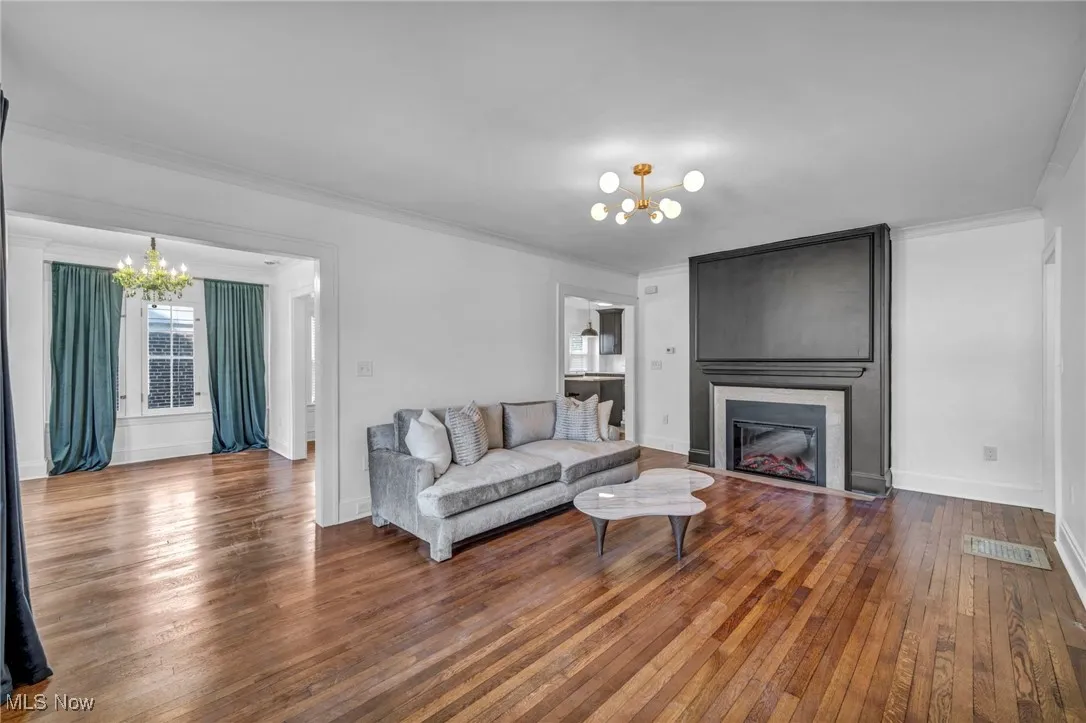 Living room featuring a chandelier, dark wood-type flooring, a large fireplace, and ornamental molding