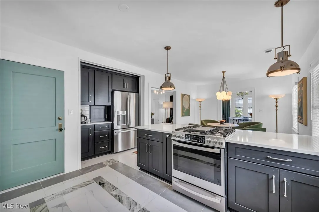 Kitchen featuring appliances with stainless steel finishes, decorative light fixtures, and light stone countertops