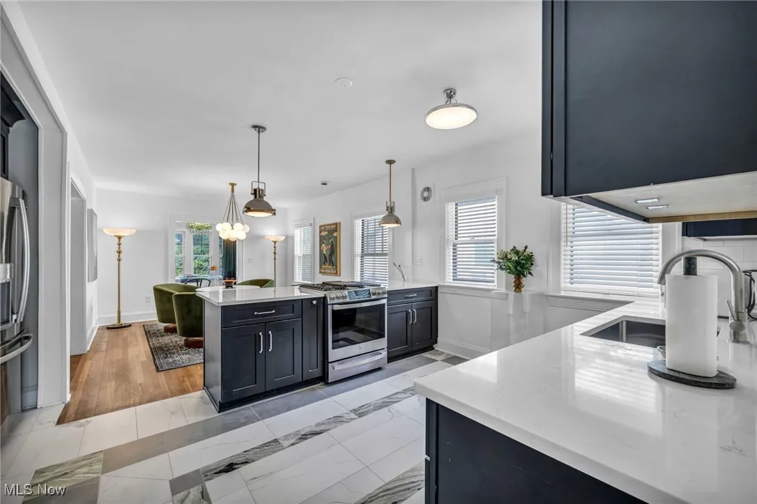 Kitchen with dark cabinetry, light stone countertops, stainless steel appliances, decorative light fixtures, and a peninsula