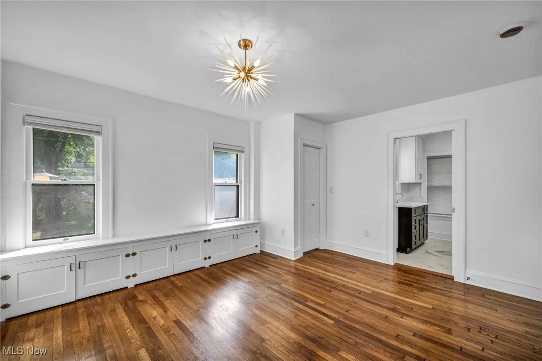 Unfurnished bedroom featuring dark wood-style flooring, multiple windows, a chandelier, and connected bathroom