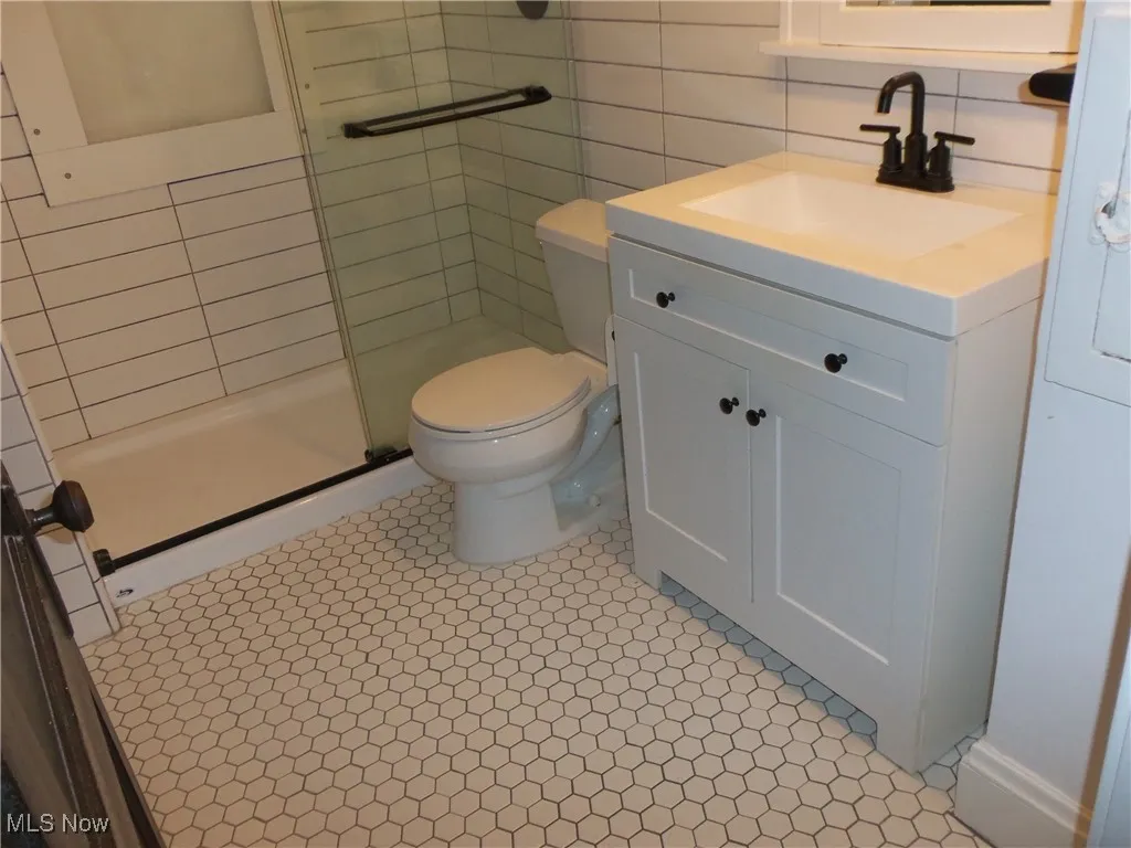 1st. Fl. Full bath featuring vanity, a shower stall, tile walls, and light tile patterned floors