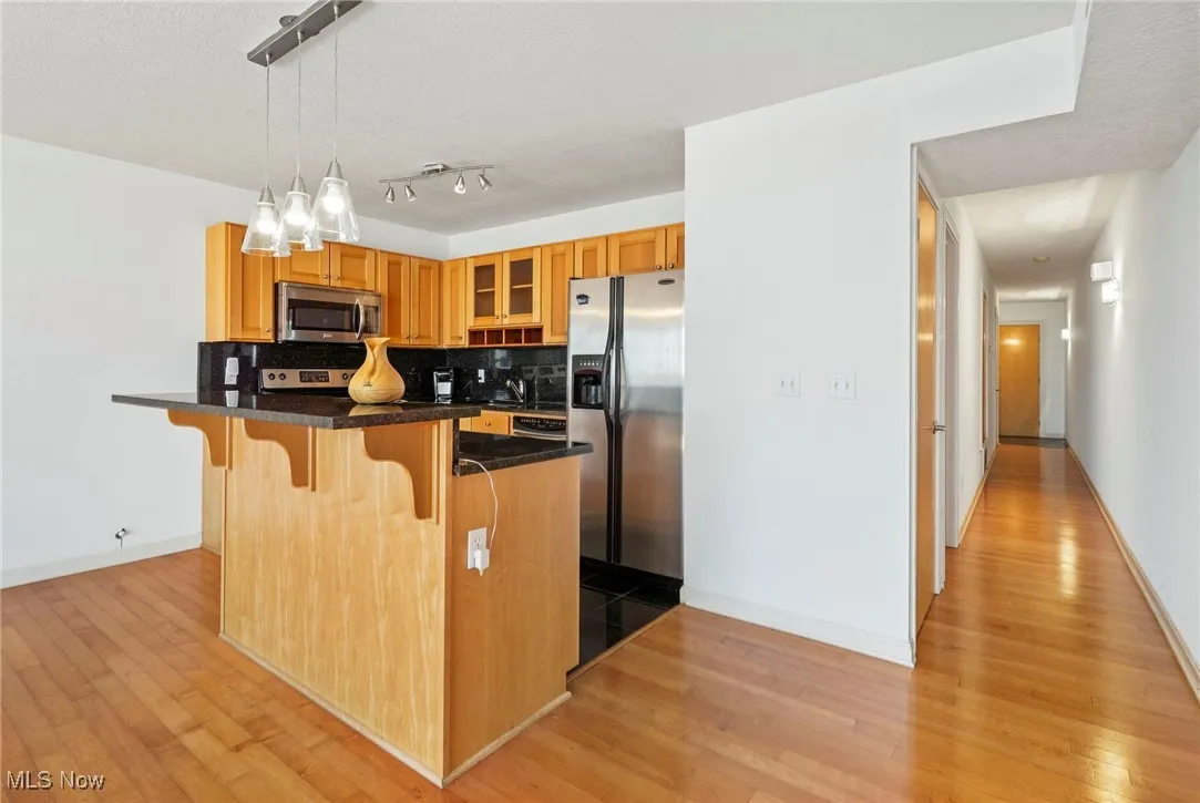 Kitchen with a kitchen breakfast bar, tasteful backsplash, appliances with stainless steel finishes, glass insert cabinets, and hanging light fixtures