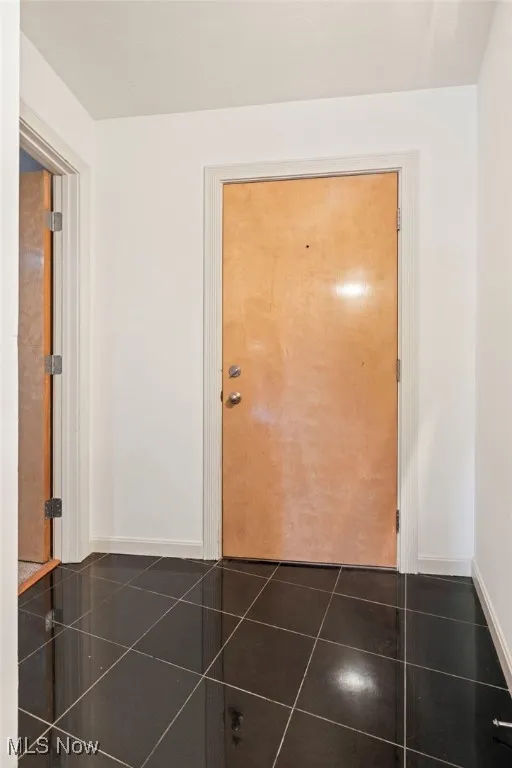 Hall featuring dark tile patterned flooring and baseboards