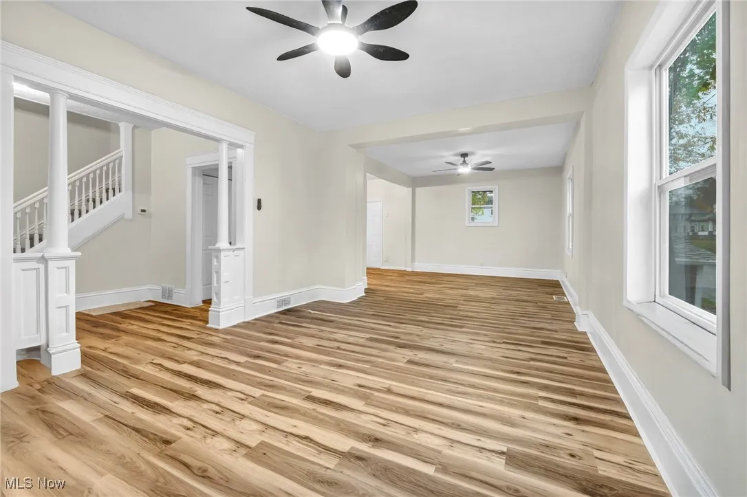 Unfurnished living room featuring light wood-style flooring, ceiling fan, and stairs