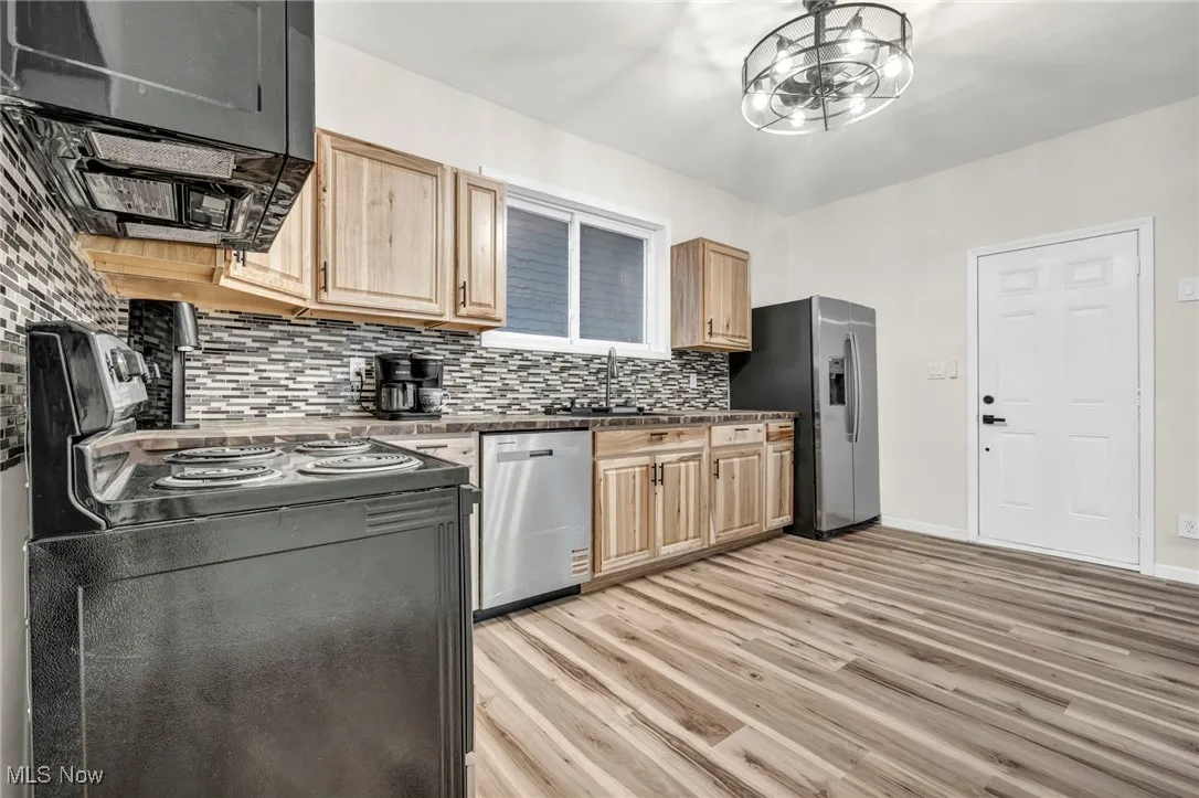 Kitchen with black appliances, light wood-type flooring, light brown cabinets, and tasteful backsplash