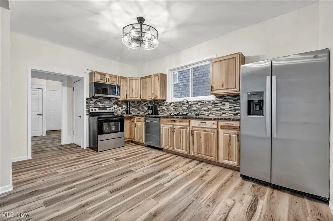 Kitchen featuring dark countertops, stainless steel appliances, light wood-style flooring, and backsplash