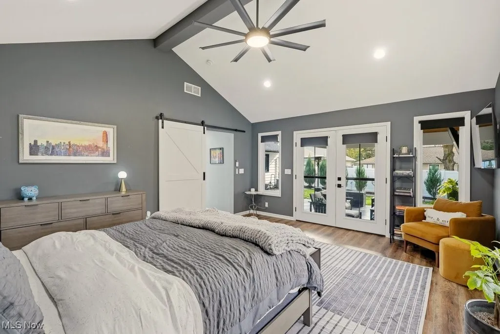 Bedroom featuring a barn door, beam ceiling, wood finished floors, access to outside, and high vaulted ceiling