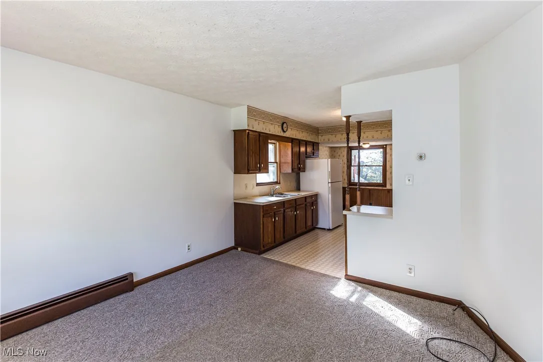 Kitchen with a baseboard heating unit, light countertops, freestanding refrigerator, a textured ceiling, and light colored carpet