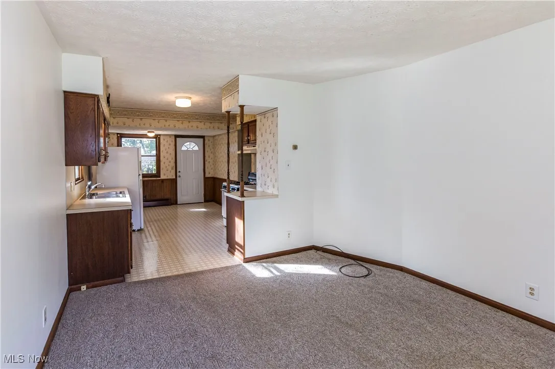 Kitchen with a textured ceiling, light countertops, light colored carpet, white appliances, and dark brown cabinetry