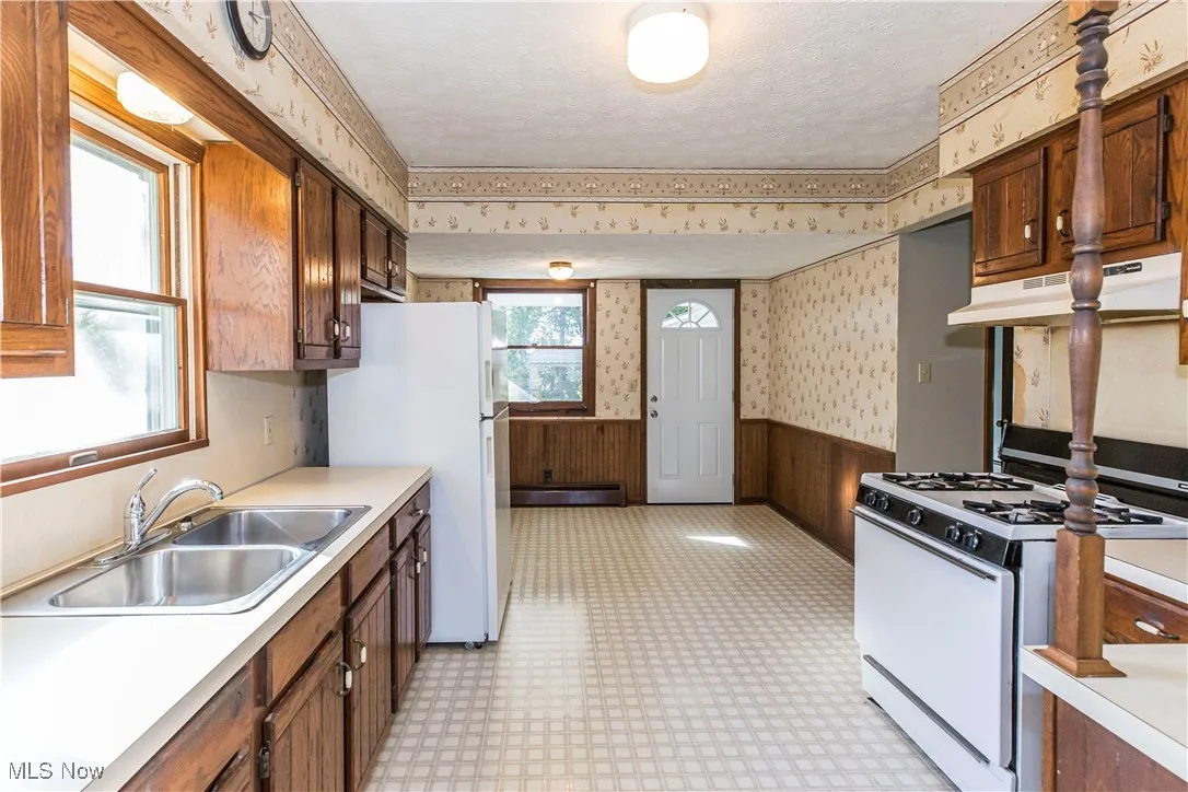 Kitchen with wainscoting, wallpapered walls, white appliances, light countertops, and wooden walls