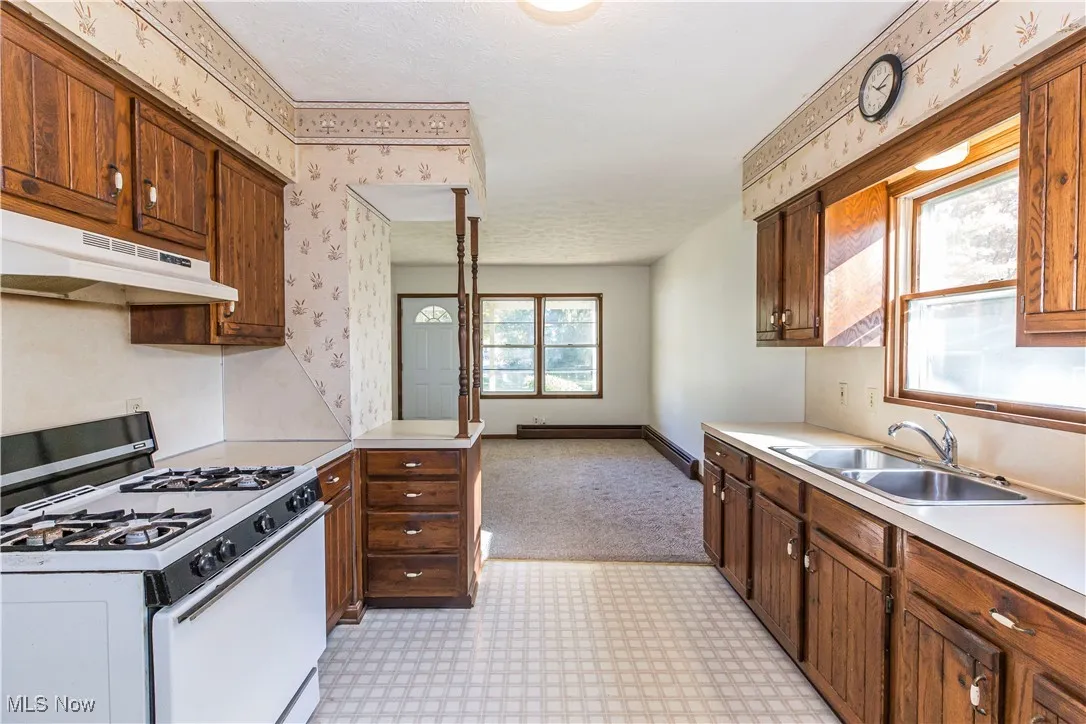 Kitchen with white gas range, under cabinet range hood, light countertops, wallpapered walls, and a peninsula