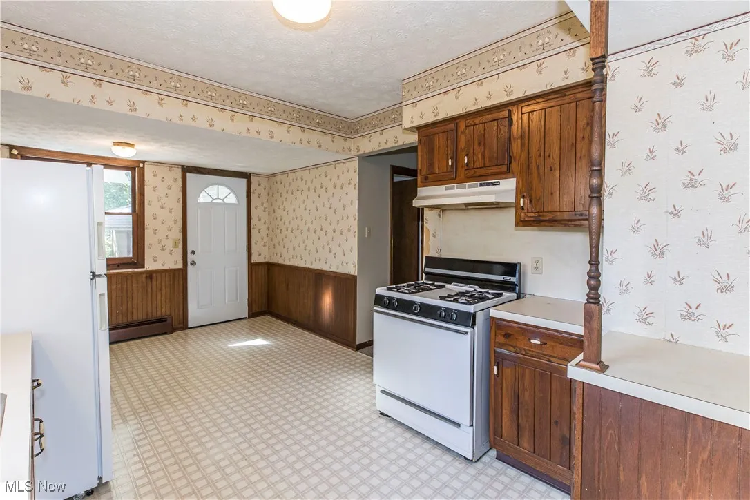 Kitchen with wainscoting, white appliances, wallpapered walls, light countertops, and wood walls