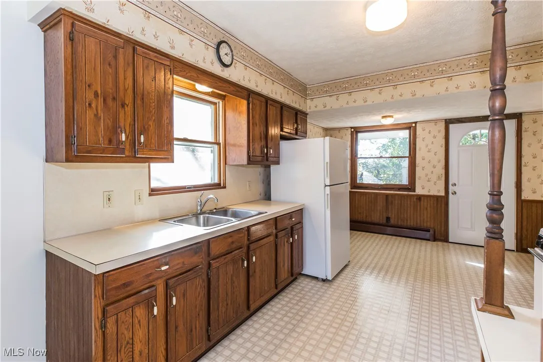 Kitchen featuring wallpapered walls, wainscoting, freestanding refrigerator, light countertops, and light flooring
