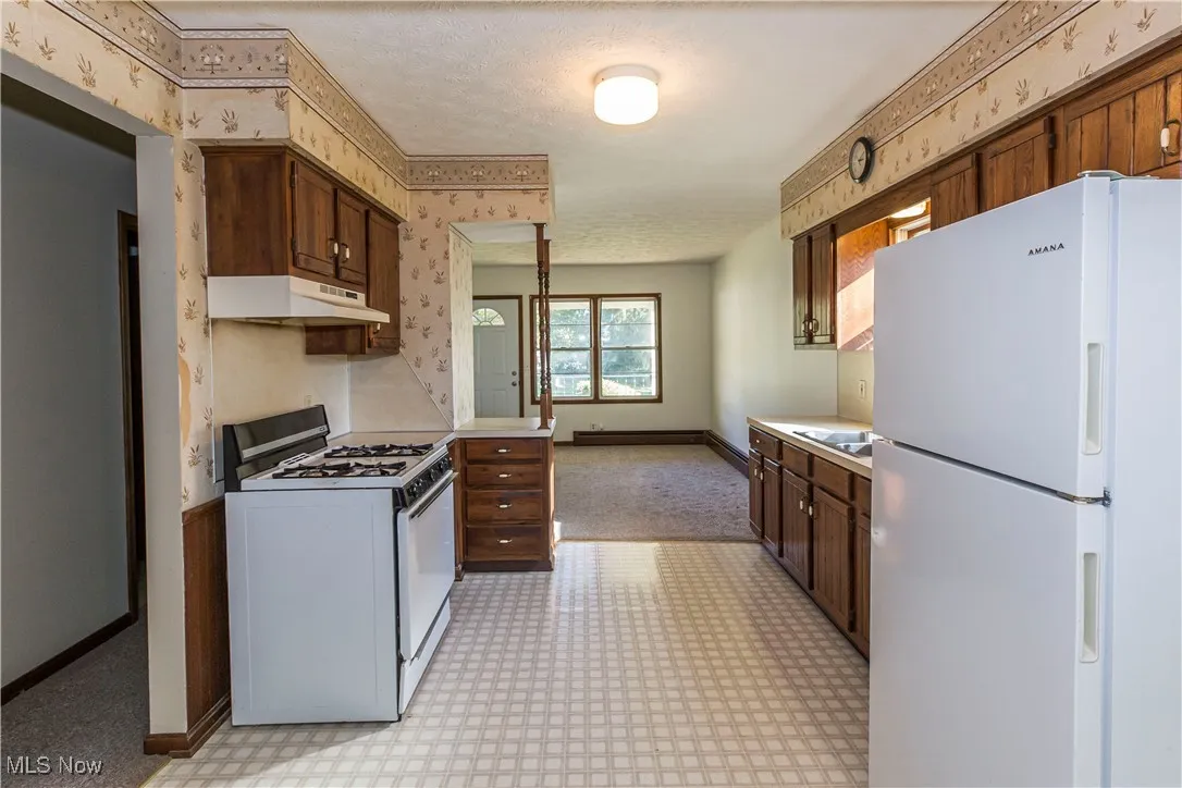 Kitchen with white appliances, light countertops, wallpapered walls, light floors, and under cabinet range hood