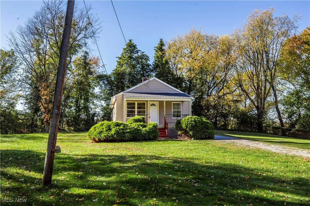 Bungalow featuring a front yard, a porch, a chimney, and view of scattered trees