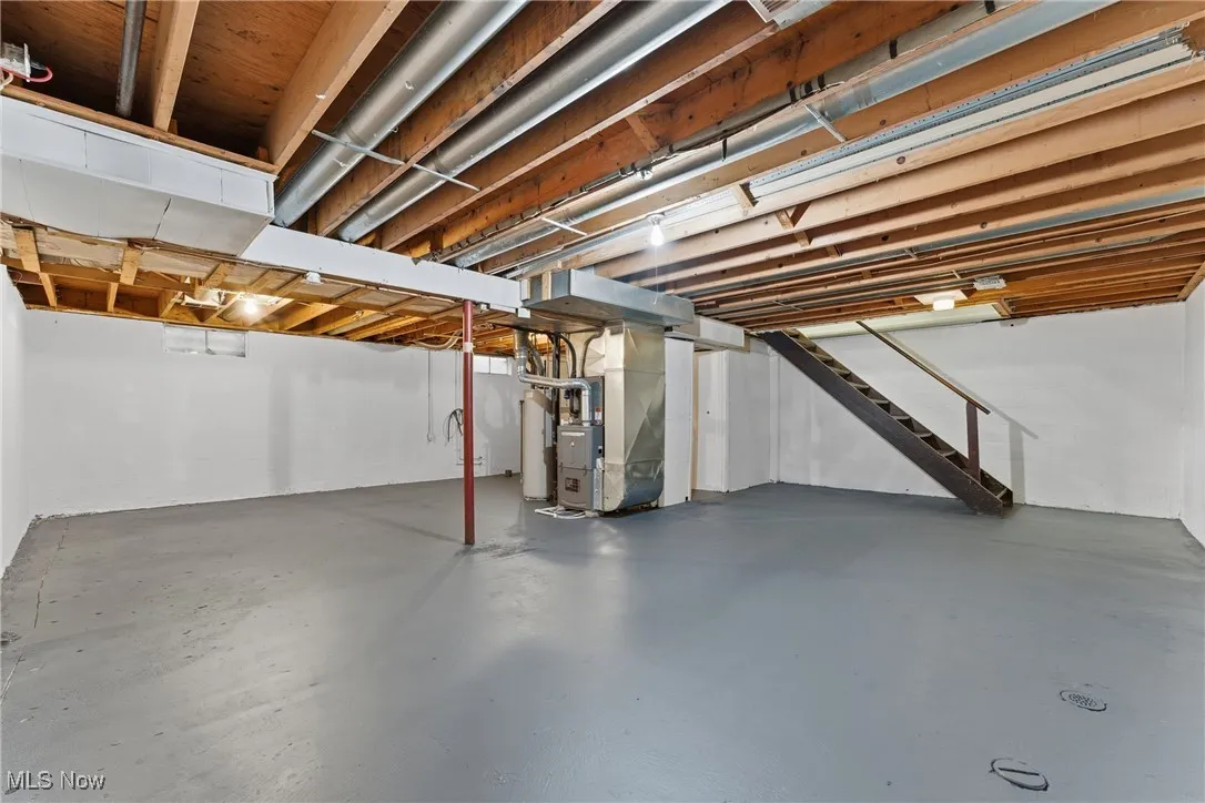 Unfinished basement featuring stairway, heating unit, and water heater