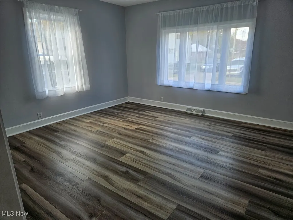 Unfurnished room with dark wood-style flooring and healthy amount of natural light