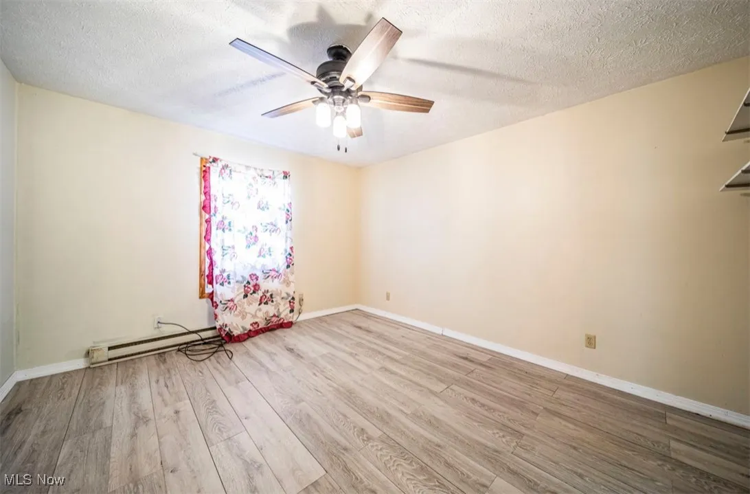 Unfurnished room featuring light wood finished floors, a baseboard heating unit, a textured ceiling, and a ceiling fan