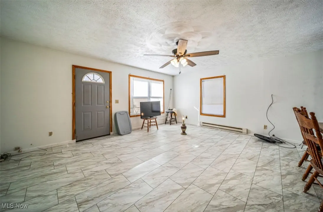Foyer entrance featuring a textured ceiling, a baseboard heating unit, light marble finish floors, and a ceiling fan