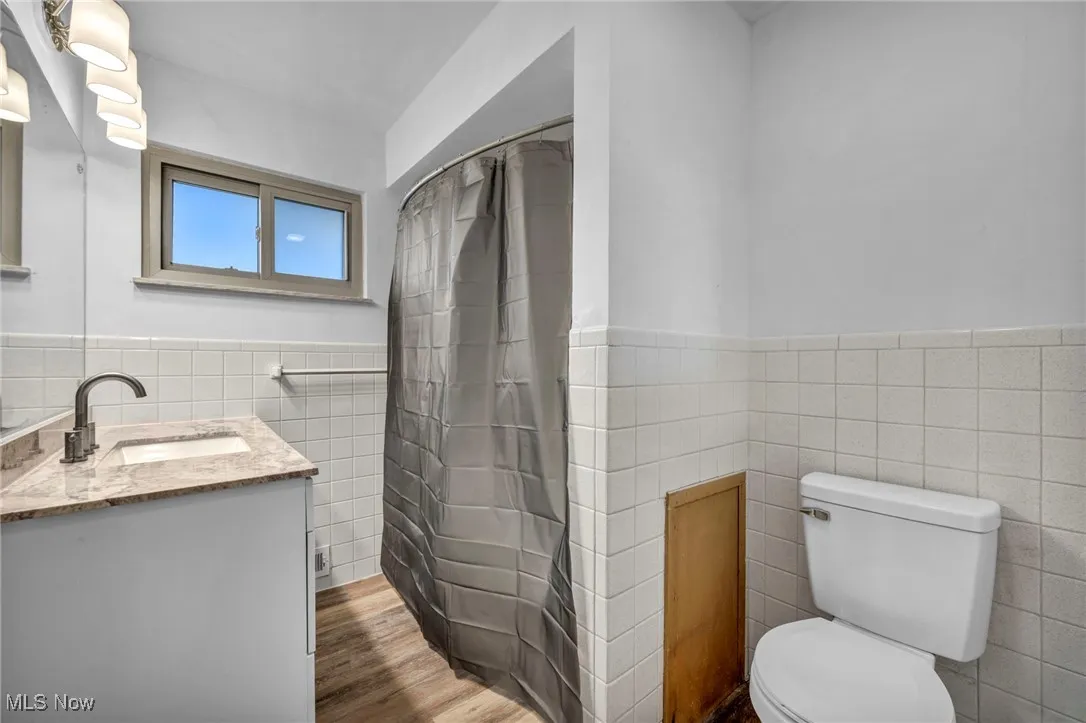Full bath featuring tile walls, vanity, wainscoting, dark wood finished floors, and curtained shower