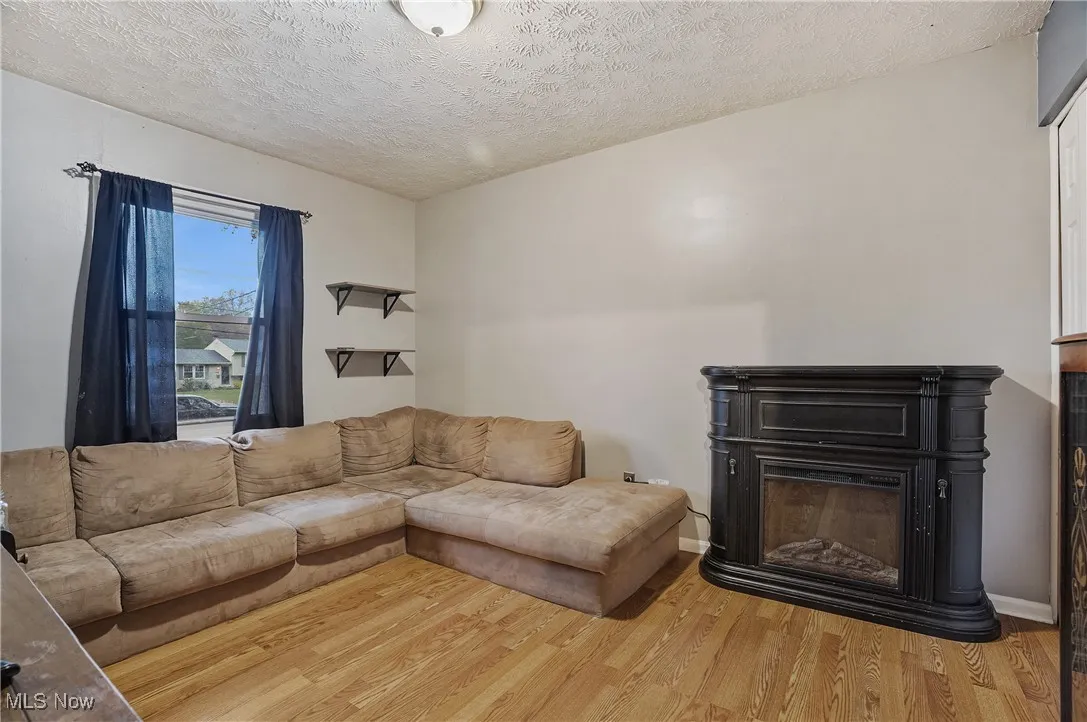 Living area with wood finished floors, a textured ceiling, and a glass covered fireplace