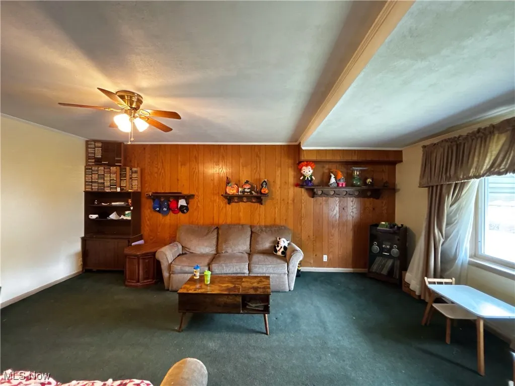 Carpeted living room featuring wooden walls and a ceiling fan
