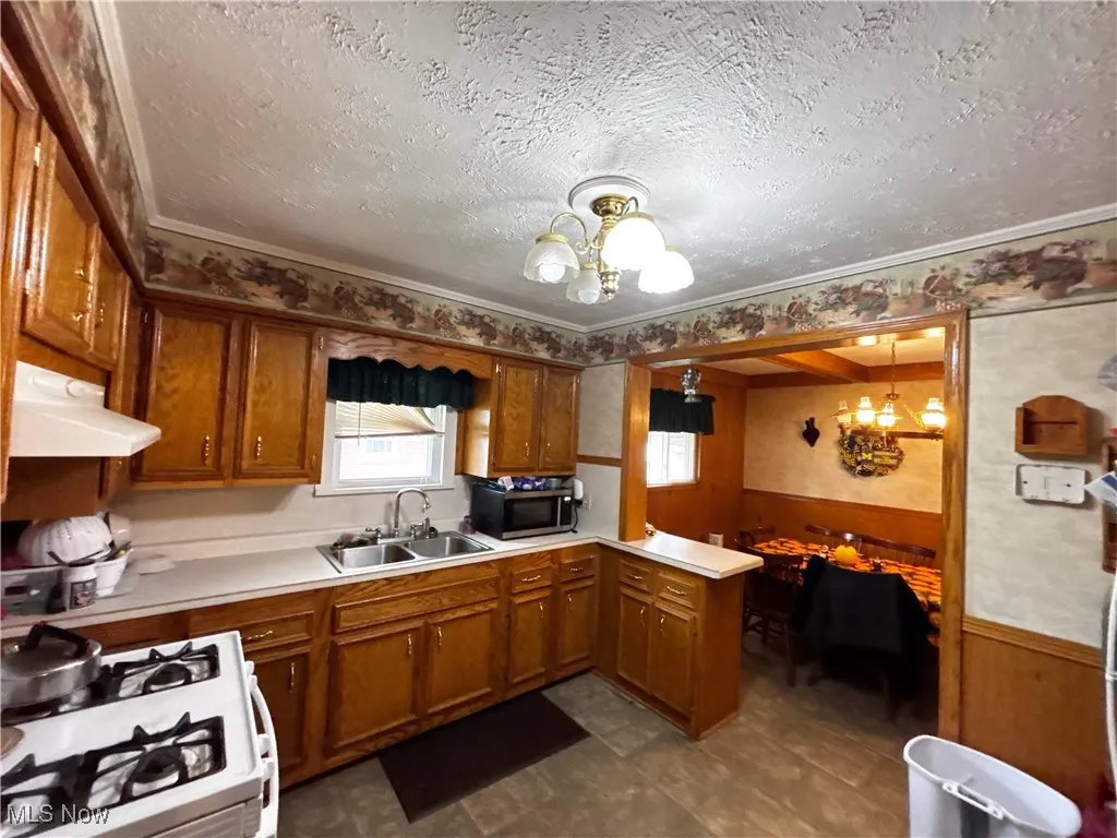 Kitchen with wainscoting, a chandelier, light countertops, white gas range oven, and a peninsula