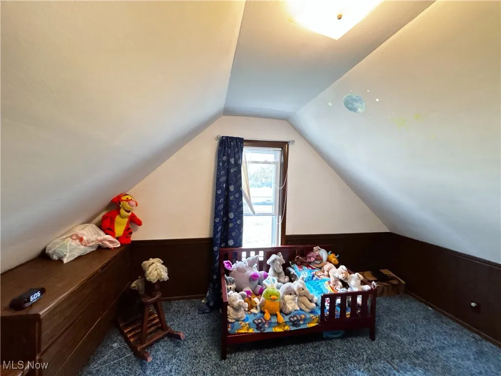 Rec room with wooden walls, wainscoting, lofted ceiling, and carpet