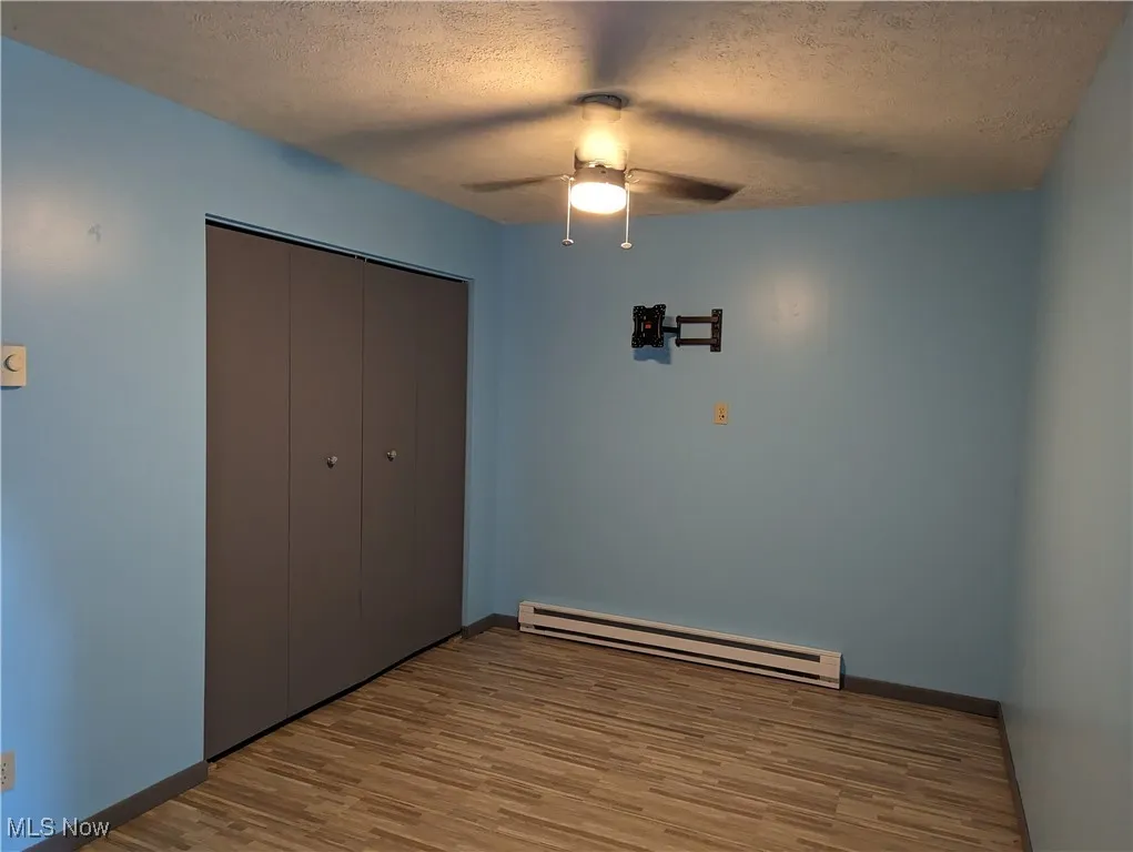 2nd view of office featuring a textured ceiling, a closet, a baseboard radiator, light wood-type flooring, and ceiling fan