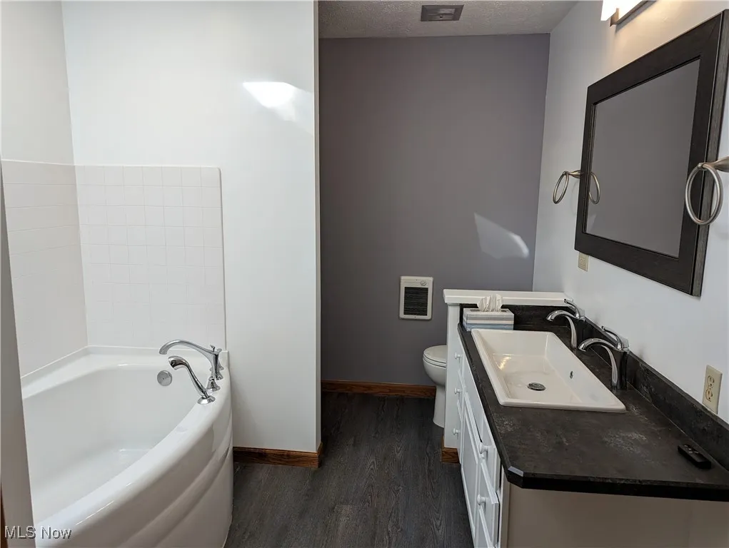Bathroom with toilet, vanity, a textured ceiling, skylight, shower stall and wood-type flooring