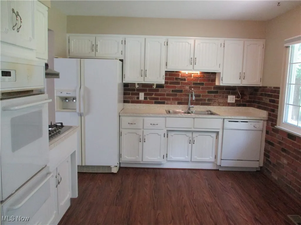 Kitchen with extractor fan, white cabinetry, dark wood-type flooring, sink, and white appliances