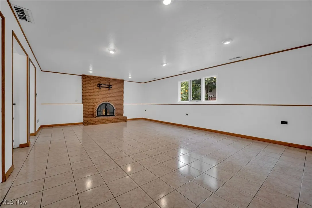 Unfurnished living room with brick wall, ornamental molding, a brick fireplace, and light tile patterned floors