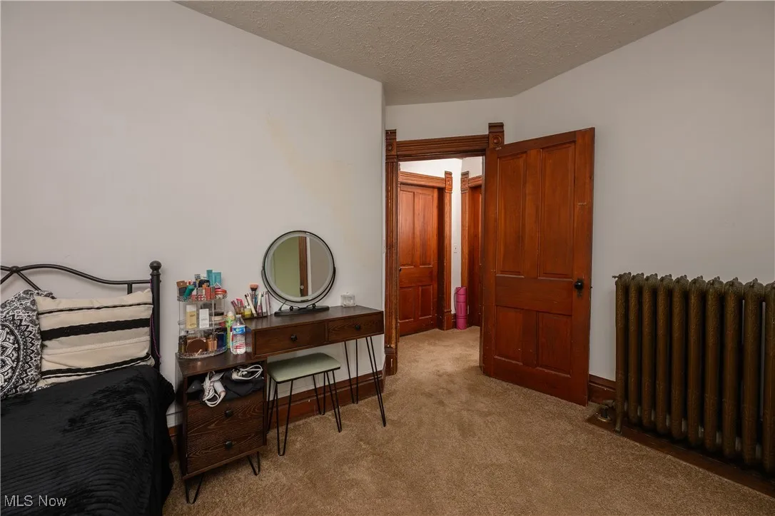 Bedroom featuring radiator heating unit, light carpet, and a textured ceiling
