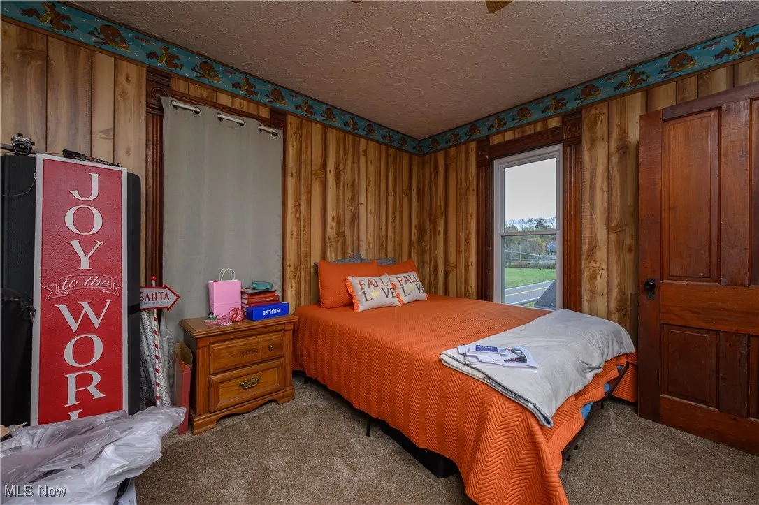 Carpeted bedroom featuring a textured ceiling and wooden walls
