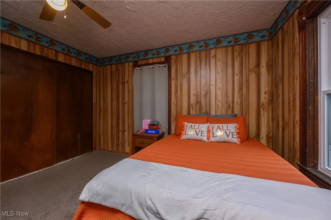Carpeted bedroom with wooden walls, a textured ceiling, and ceiling fan