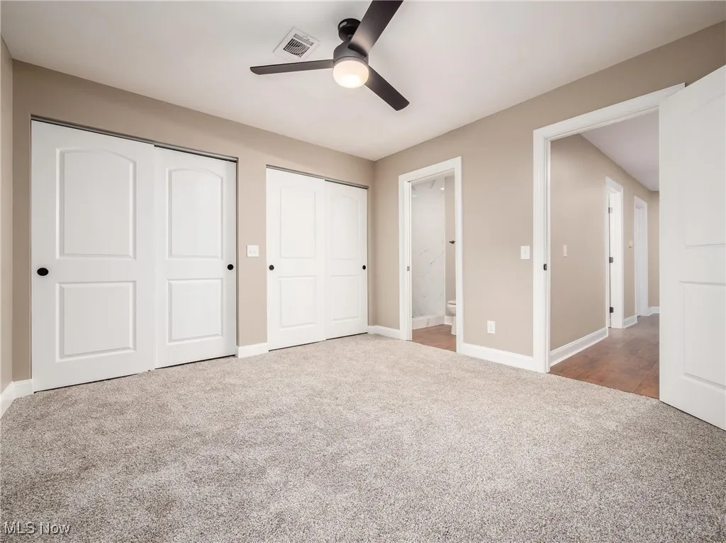Unfurnished bedroom featuring multiple closets, light carpet, ceiling fan, and ensuite bathroom