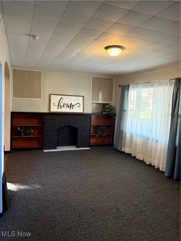 Living room with dark carpet, a decorative only fireplace, and arched walkways