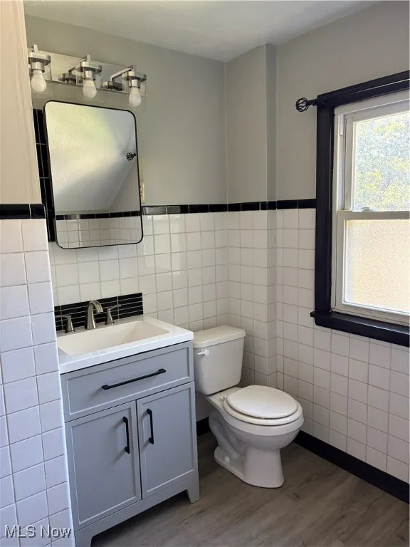 Bathroom featuring tile walls, vanity, wood finished LVT floors