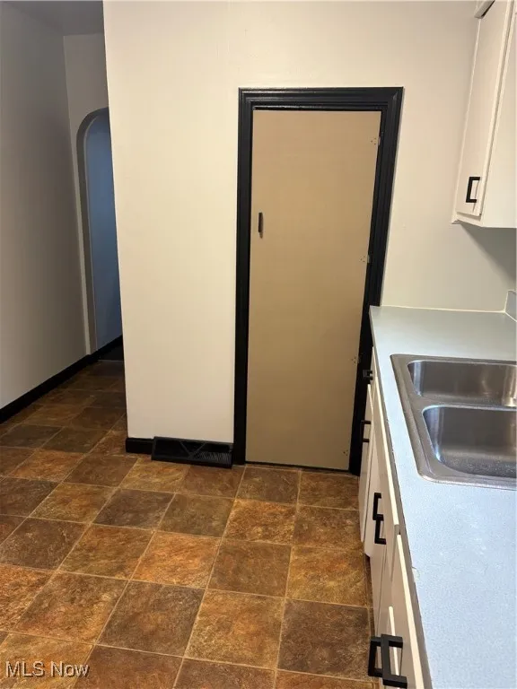 Kitchen with white cabinetry, light countertops, arched walkways, pantry and stone finish vinyl flooring