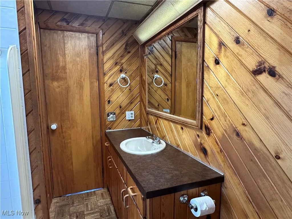 Half bathroom with vanity, wooden walls, and a drop ceiling
